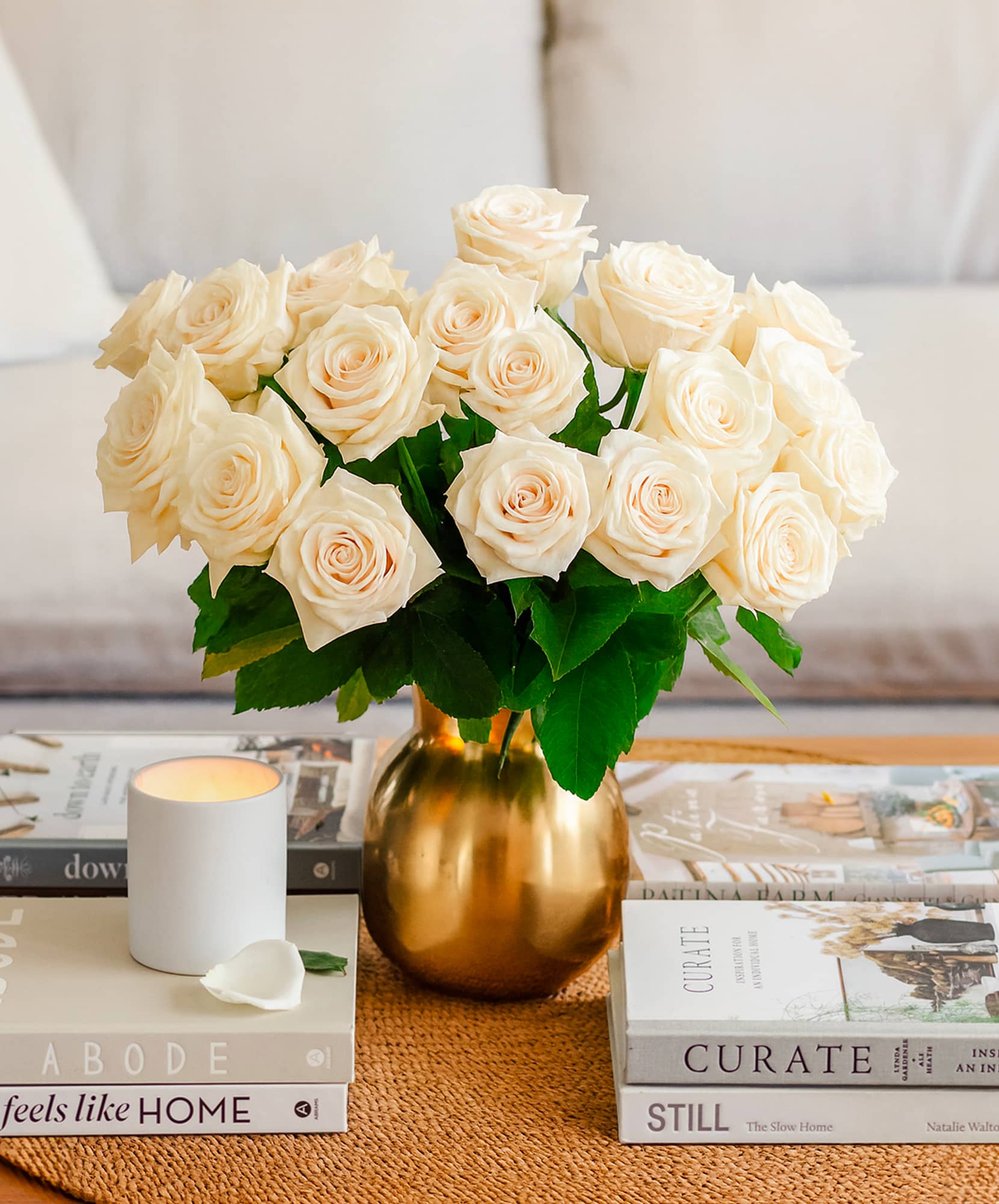 Elegant white roses in a gold vase, surrounded by stylish coffee table books and a candle.